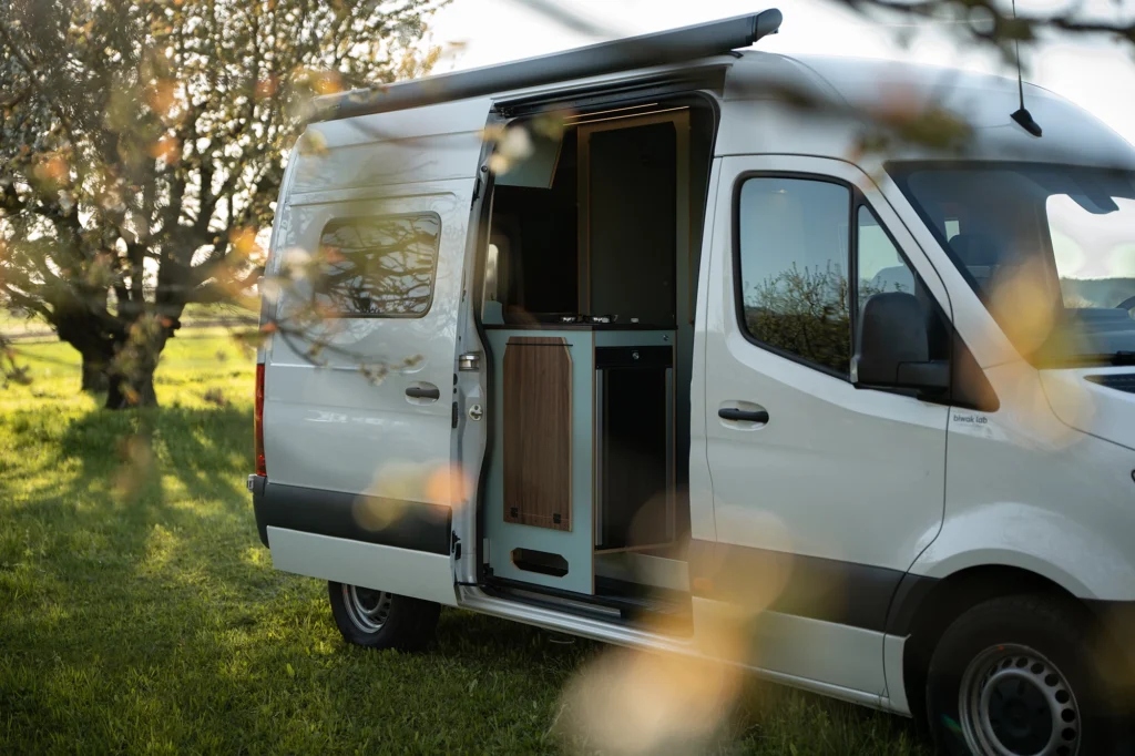 Camper Ausbau Mercedes Sprinter mit modernem Innenausbau und Markise in der Natur