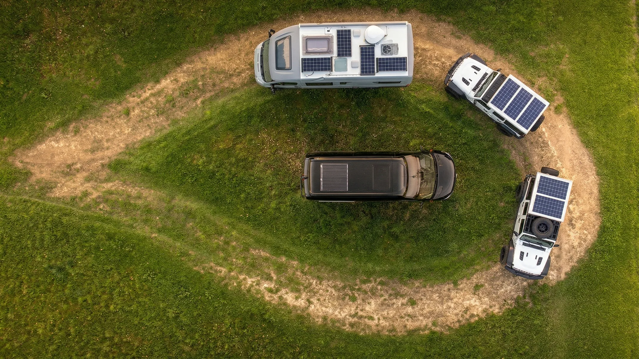 Luftaufnahme mehrerer individuell ausgebauter Camper mit Solarpanels auf einem Rundweg in der Natur – moderner Camperausbau Schweiz für autarkes Reisen