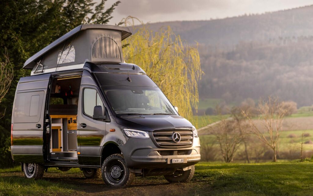 Mercedes Sprinter Camper von BiwakLab mit Aufstelldach und geöffnetem Seitenzugang, perfekt für autarkes Reisen und Outdoor Abenteuer
