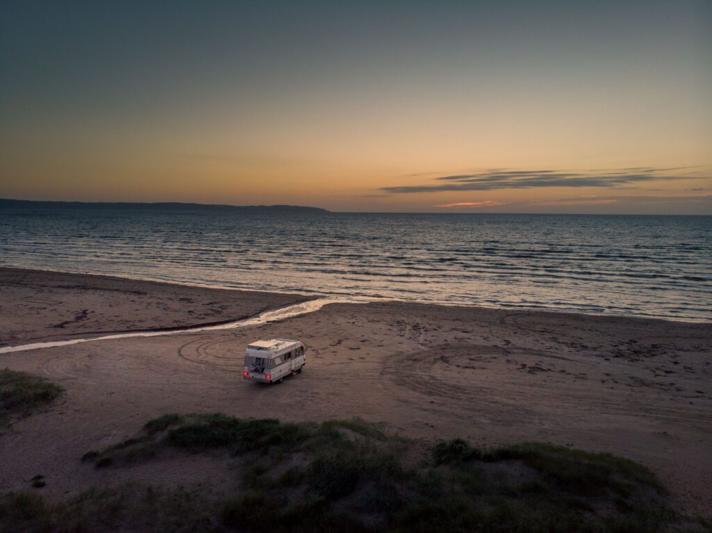 Wohnmobil mit Solaranlage steht bei Sonnenuntergang direkt am Strand. Autarkes Reisen mit Solarenergie ermöglicht unabhängige Stromversorgung für das Wohnmobil inmitten einer ruhigen Küstenlandschaft.